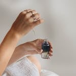 A close-up of hands holding a glass bottle with blue liquid, using a pipette.