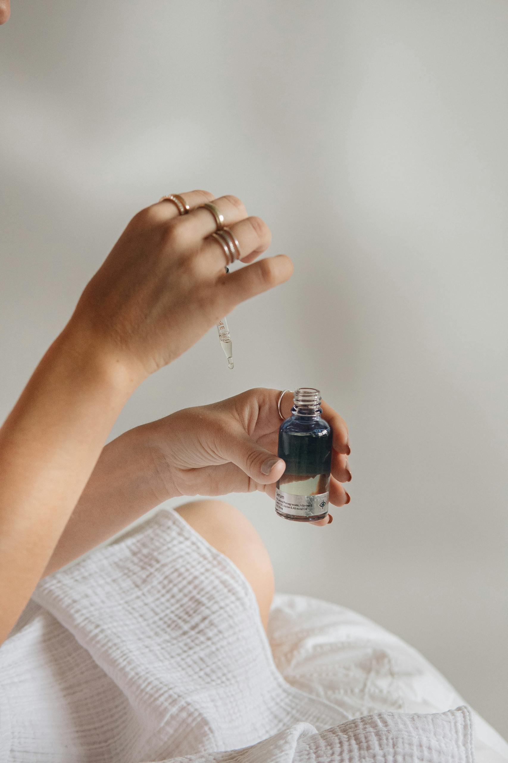 A close-up of hands holding a glass bottle with blue liquid, using a pipette.