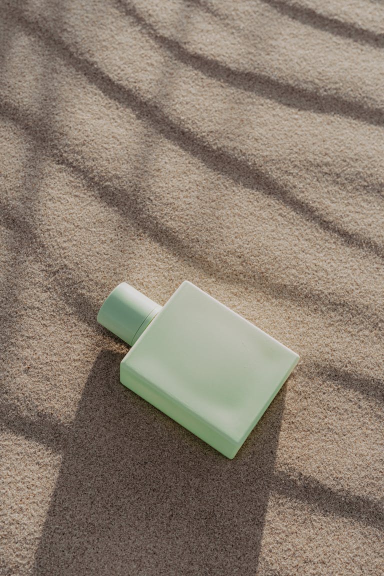 Elegant green perfume bottle resting on textured sand, evoking a serene and natural aesthetic.