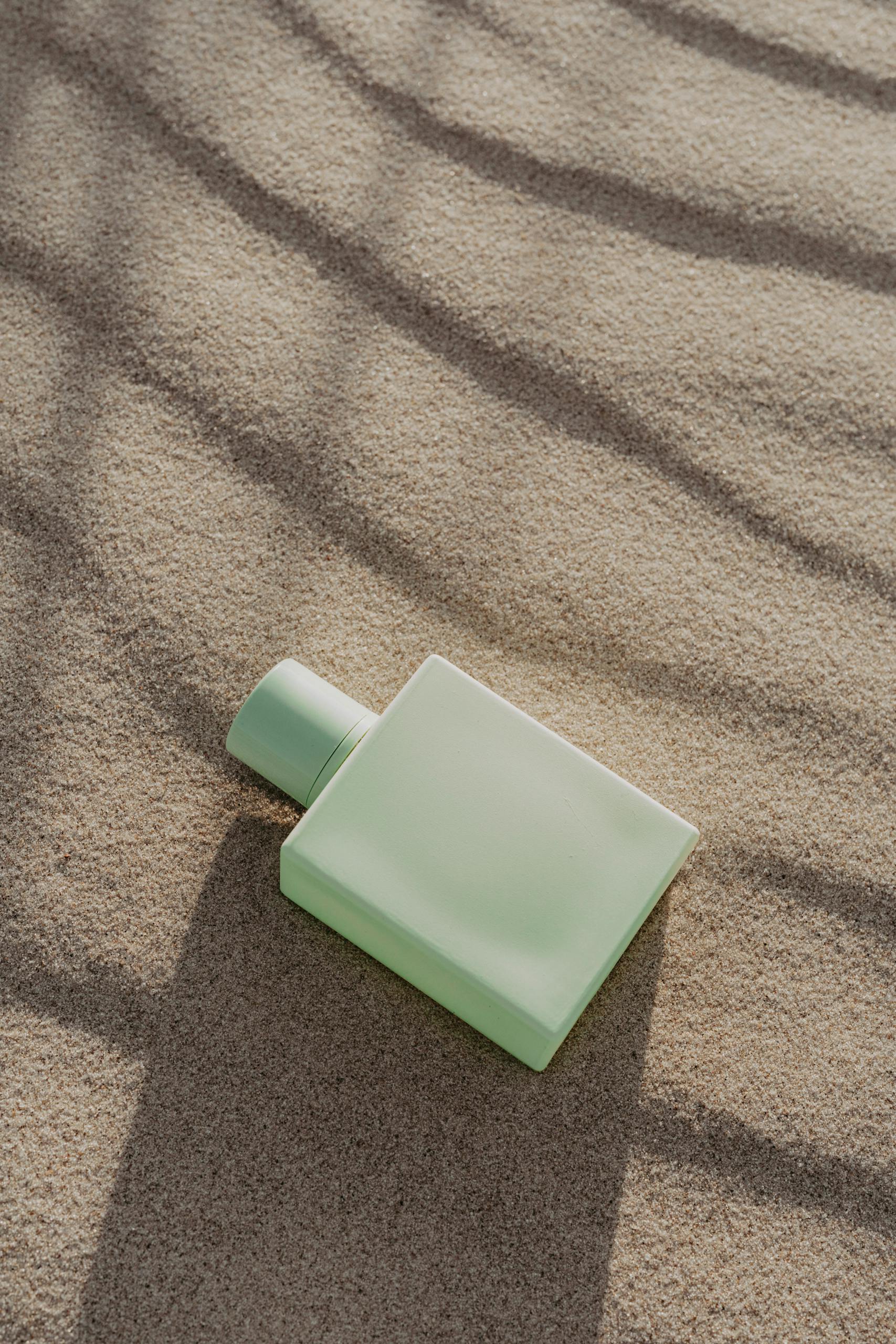 Elegant green perfume bottle resting on textured sand, evoking a serene and natural aesthetic.