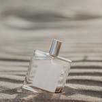 Minimalist glass perfume bottle on sand, evoking a fresh and beachy fragrance vibe.