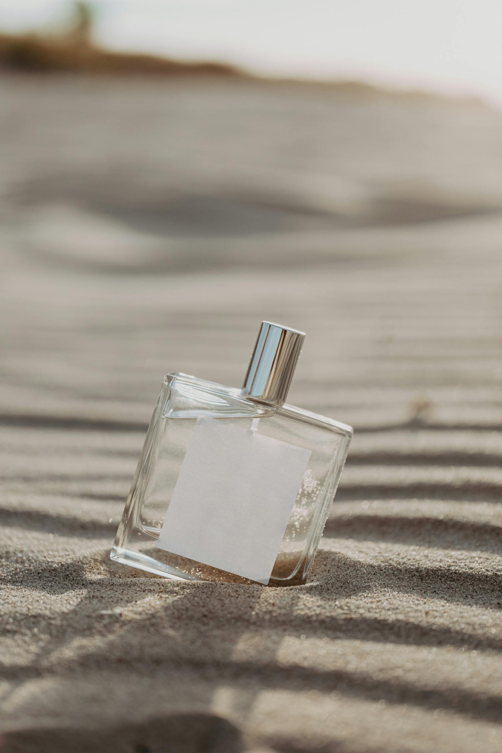 Minimalist glass perfume bottle on sand, evoking a fresh and beachy fragrance vibe.