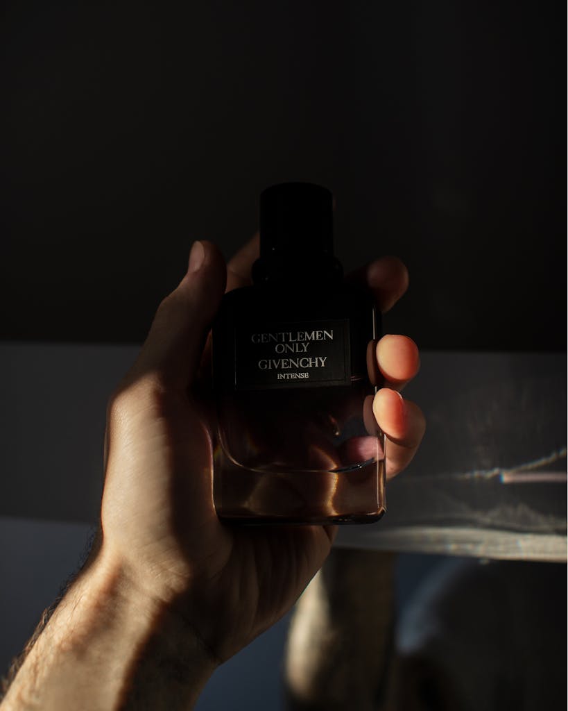 A man's hand holds a Givenchy perfume bottle with dramatic lighting.