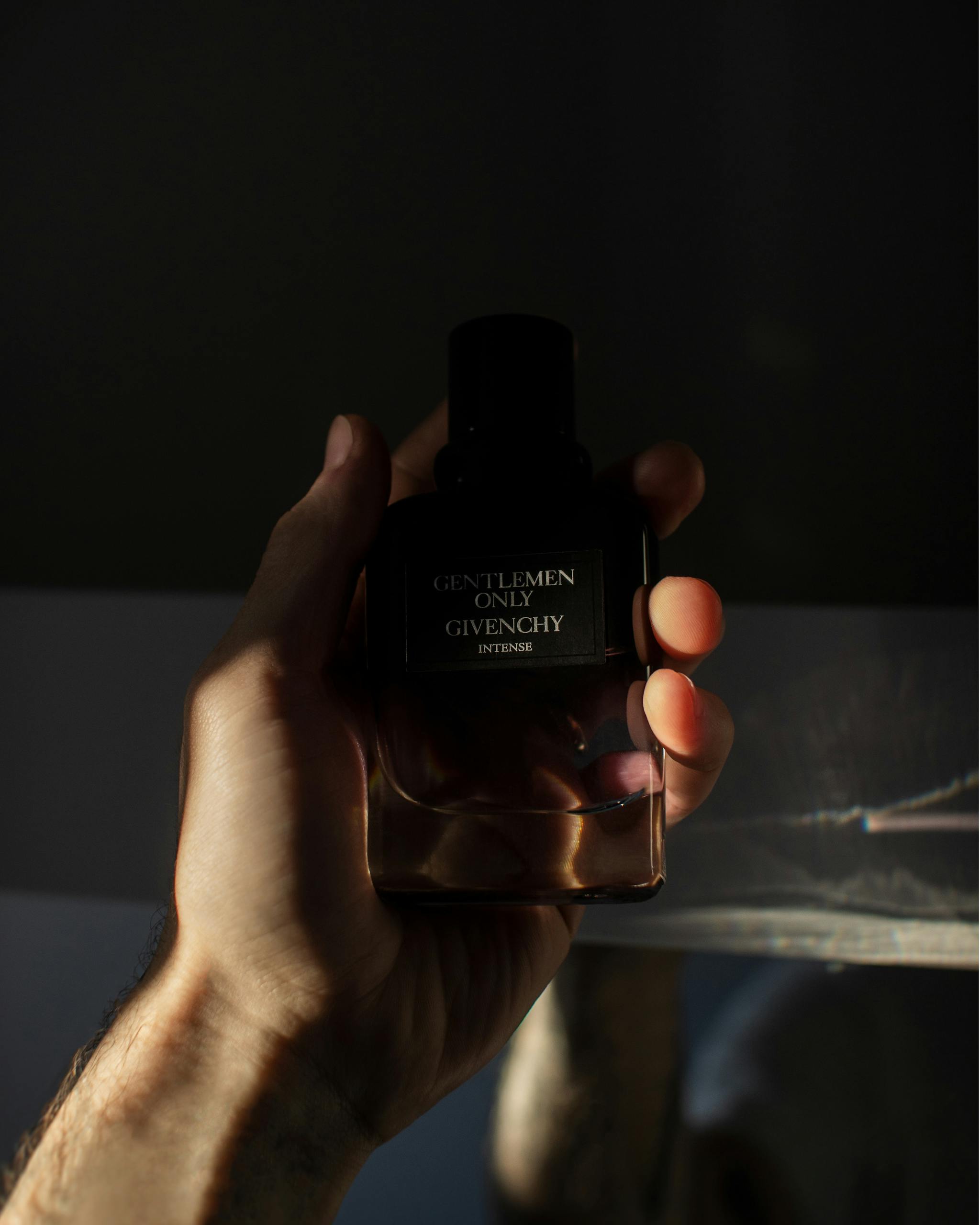 A man's hand holds a Givenchy perfume bottle with dramatic lighting.