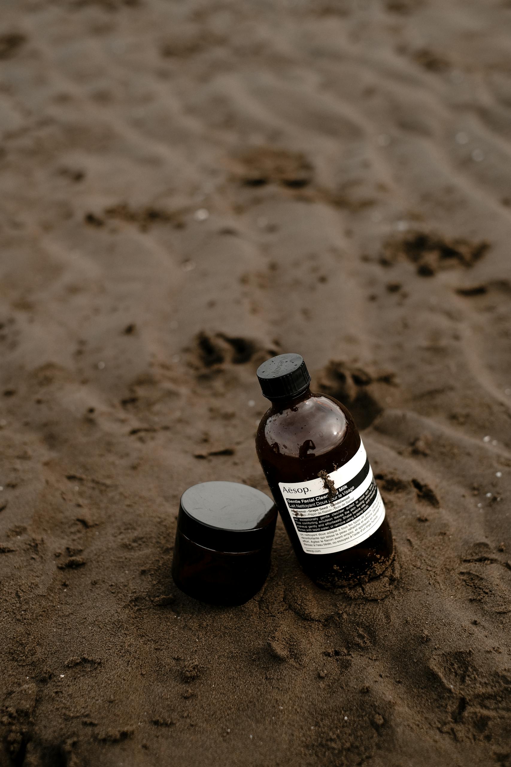 Brown bottles of cosmetic products placed on a sandy beach, conveying a natural and eco-friendly vibe.