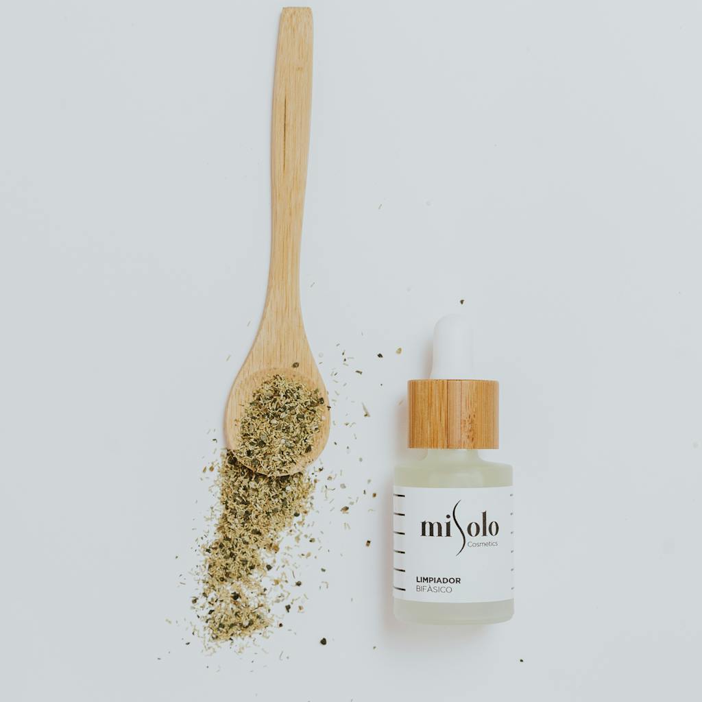 Qutane Pré-Soins Apaisant Flat lay of a natural skincare bottle with herbs and wooden spoon on a white background.